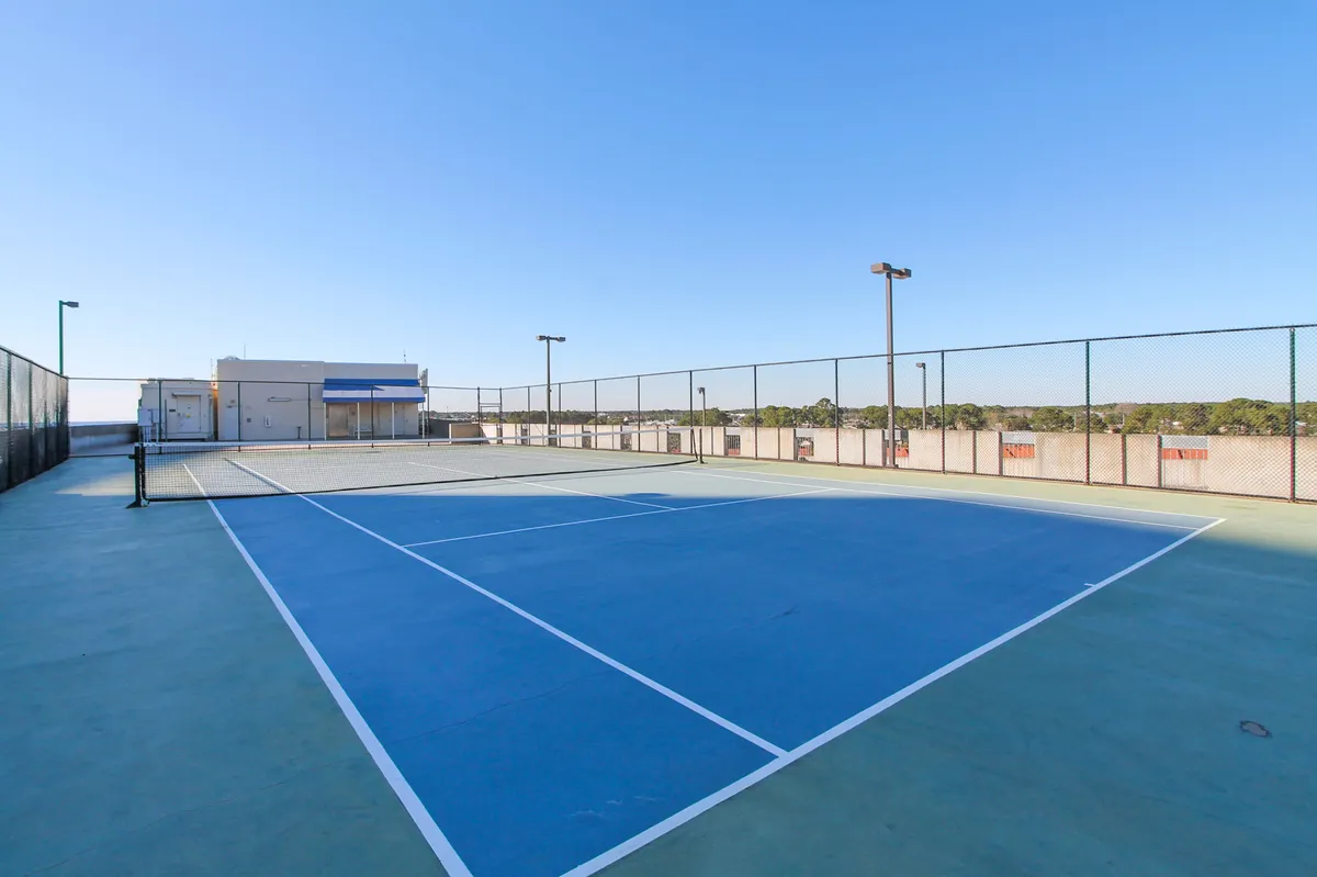An active tennis court framed by lush greenery and open skies, capturing the spirit of outdoor recreation and wellness. The clean lines and energetic mood echo a commitment to health and social play.