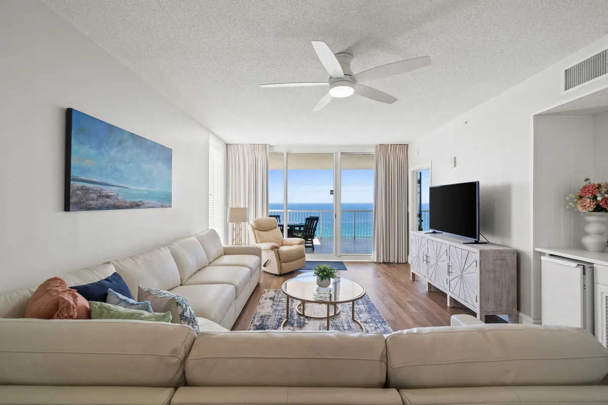 A living area with a comfortable white sofa and a coffee table adorned with decorative items. Large windows frame a sweeping ocean vista, while a sleek TV unit with a flat-screen offers entertainment options. The atmosphere is calm and serene, ideal for unwinding with loved ones.