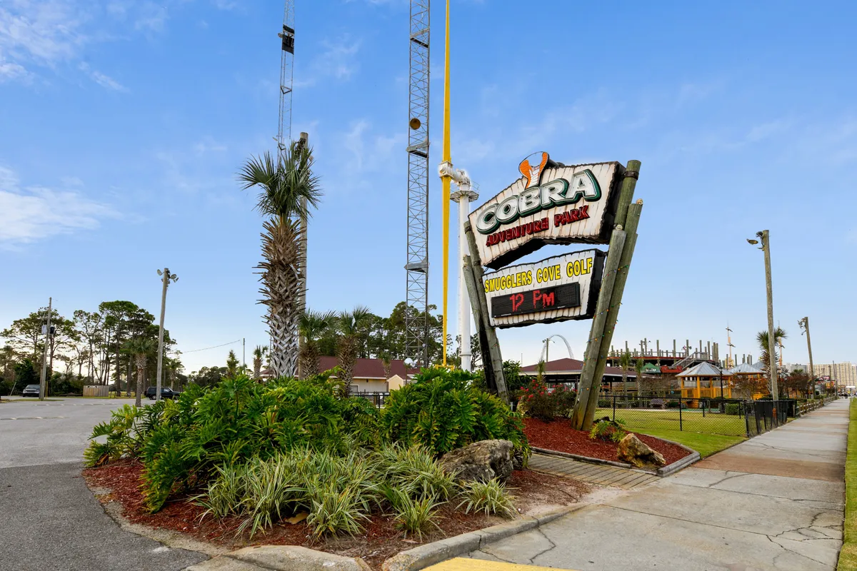 An exterior shot focused on the Cobra Adventure Park sign, surrounded by lush greenery, playground equipment, and a mini-golf area. Families are visible enjoying mini-golf and outdoor adventures, showcasing an environment perfect for group fun and memorable outings.