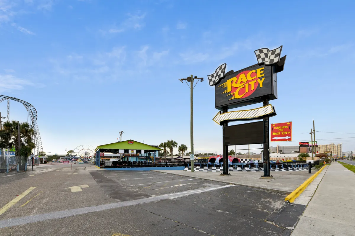 An exterior photo capturing the iconic Race City sign, a go-kart track, and a Ferris wheel, with people visible in the seating area. The scene buzzes with energy and excitement, perfect for family outings and amusement park thrills.