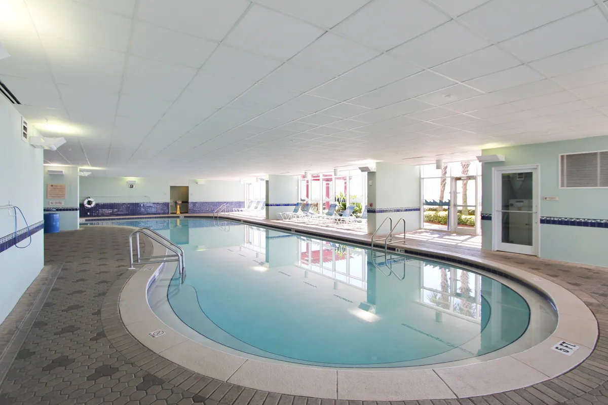 A serene indoor pool area featuring modern lounge chairs and large windows that allow natural light to fill the space. The inviting atmosphere is perfect for relaxing, swimming, or socializing with friends and family.