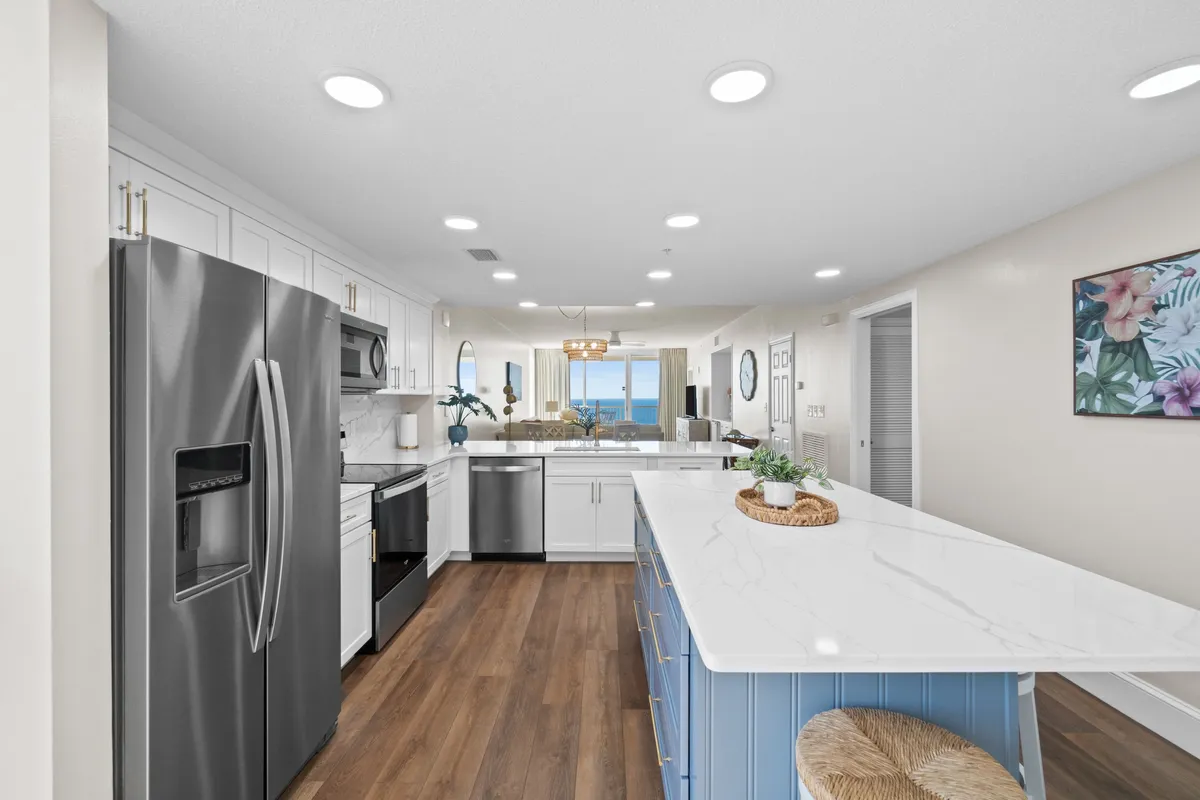 A contemporary kitchen island takes center stage, surrounded by sleek stainless steel appliances and decorative artwork. Large windows frame breathtaking ocean views, infusing the space with natural light. The open layout invites both cooking and socializing.