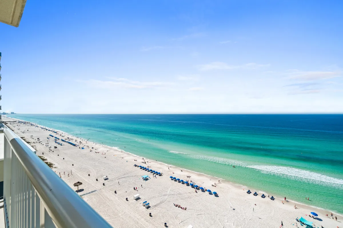 A tranquil beachfront scene with a wide expanse of sand, calm blue ocean, and sun umbrellas. The area looks peaceful and inviting, ideal for sunbathing, swimming, or sunset strolls along the shore.