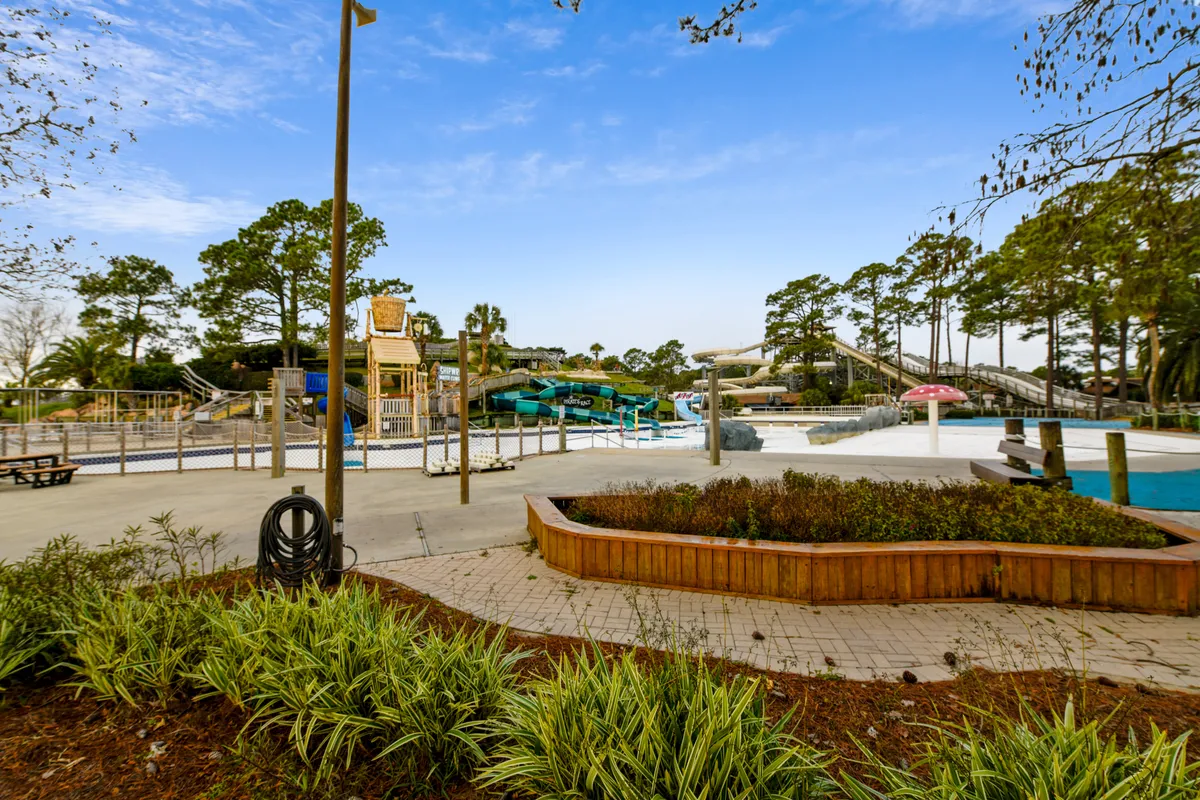 A vibrant outdoor pool area with twisting water slides, a playground, and landscaped gathering spaces. Families are seen enjoying the pool and playground, capturing the energy and fun of shared resort experiences.