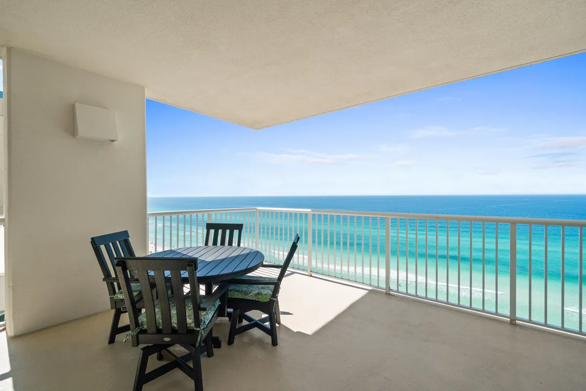 An expansive balcony with a round outdoor dining table and four chairs, framed by white railings. The balcony overlooks a panoramic view of the Gulf of Mexico, providing a tranquil setting for morning coffee, sunset drinks, or meals in the fresh air.