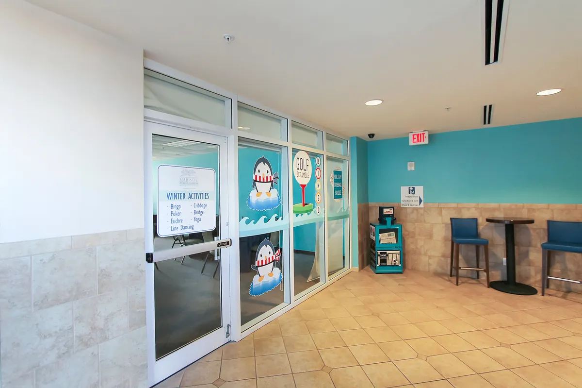 A colorful, playful interior space features winter activities signage, wall art with penguins and a golf theme, a cozy seating area, and a rack with brochures and activity information. The area exudes a welcoming vibe, hinting at the resort's rotating guest activities and social spaces for all ages.
