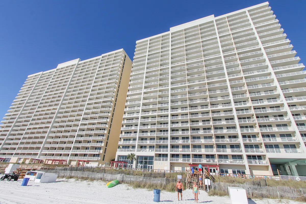 A wide view of the Majestic Beach Resort high-rise with multiple balconies overlooking a private sandy beach. Guests are seen enjoying the beach directly in front of the resort, highlighting easy access to both the ocean and resort amenities.